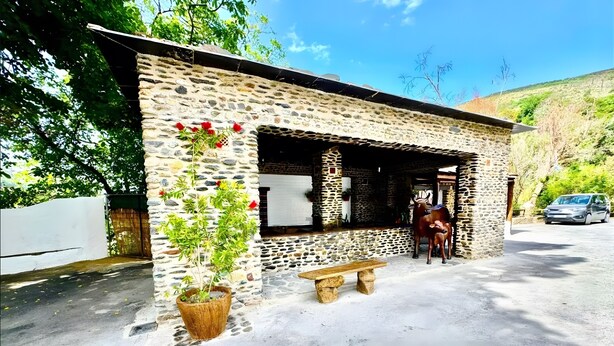 A stone building with a bench, a horse statue, and a car parked outside. - Apartment 'Rey Melchor' with Mountain View, Private Terrace and Wi-Fi (Trevélez)