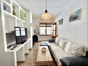 Una sala de estar con televisor, sofá, mesa de centro y estantes con objetos decorativos.