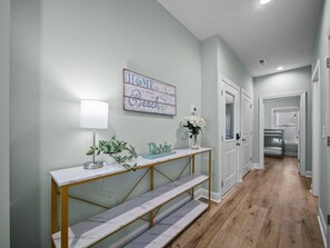 Um corredor com um aparador, uma luminária, uma placa decorativa e uma cama beliche ao fundo.