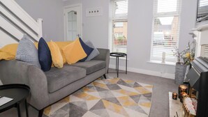 A living room with a grey sofa, yellow and blue cushions, a geometric patterned rug, a small black side table, and a fireplace with candles. - 127 Bellhouse Way (York)
