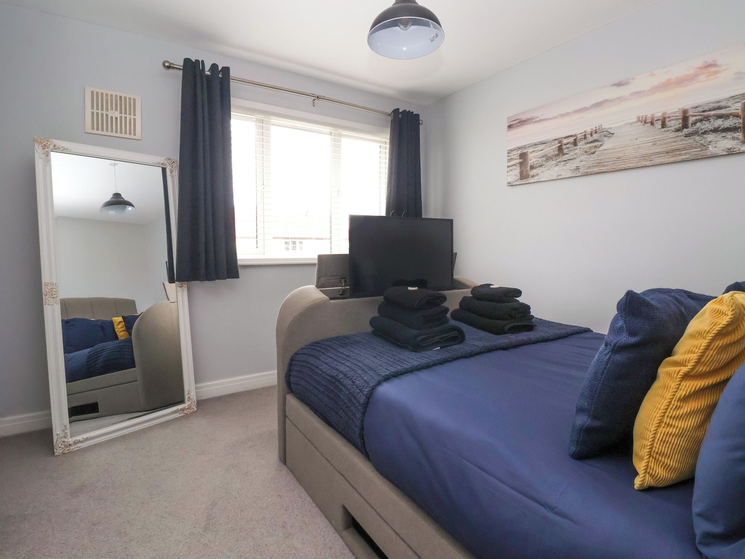 A bedroom with a bed, a TV, a mirror, and a window with curtains.