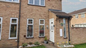 A two-story brick house with a front door, a small garden with flowers, and a visible number '127' on the wall. - 127 Bellhouse Way (York)