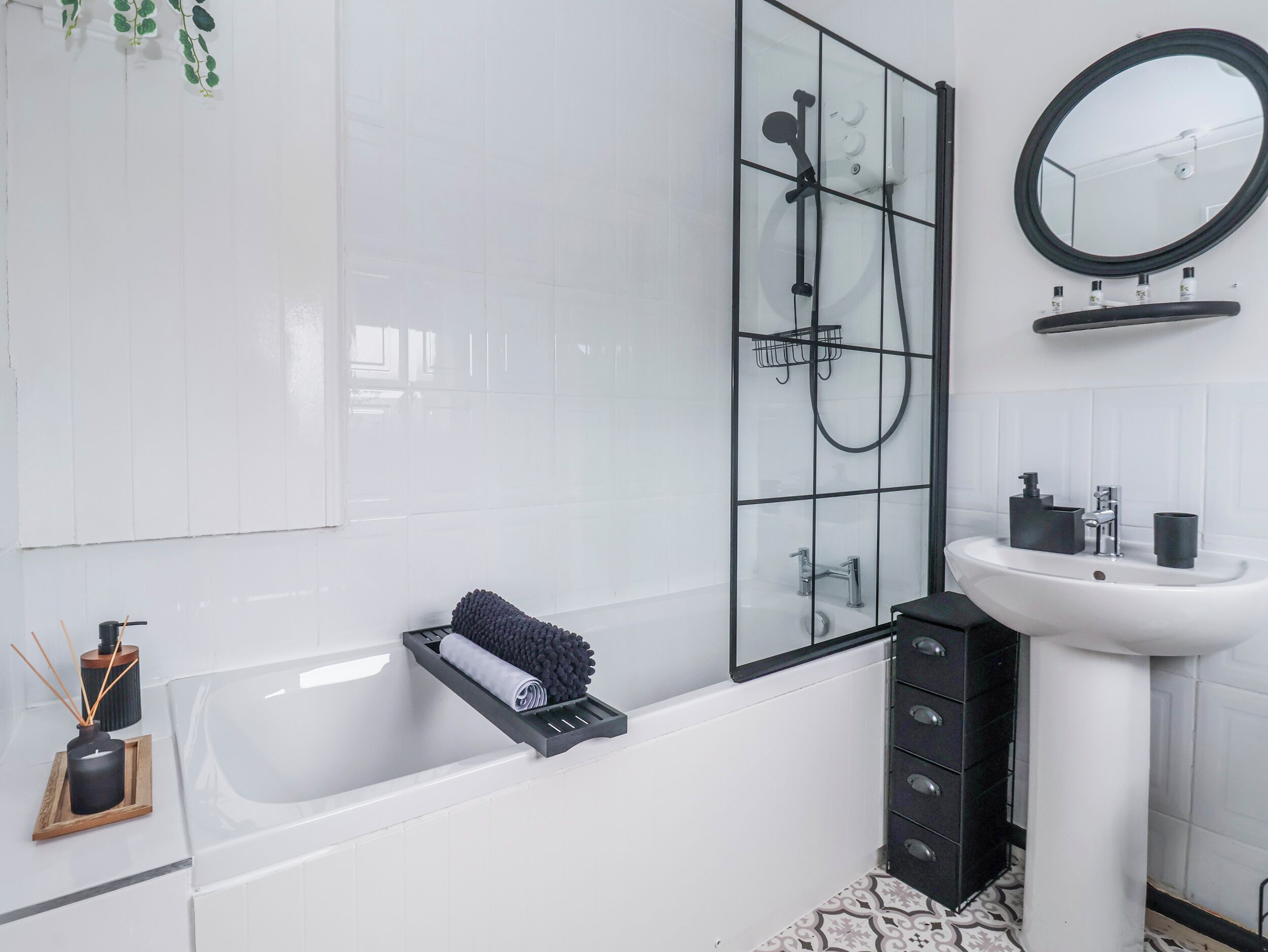 Un bagno moderno con box doccia in vetro, una vasca da bagno bianca, un porta asciugamani nero, un lavandino bianco e uno specchio.