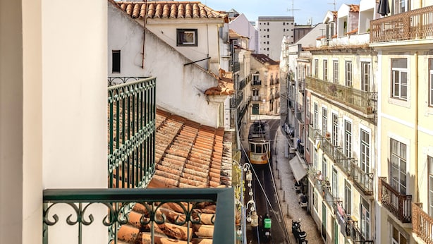 A narrow street with buildings on either side, a tram in the middle, and a balcony with a metal railing. - S O Bento Modern by Homing (Lisbon)