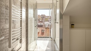 A modern bathroom with a shower, a view of the city through the glass door, and a small shelf with a plant. - S O Bento Modern by Homing (Lisbon)