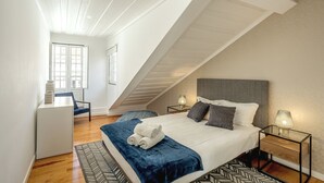 A modern bedroom with a sloped ceiling, a large bed with a grey headboard, two bedside lamps, and a small desk with a chair. - S O Bento Modern by Homing (Lisbon)