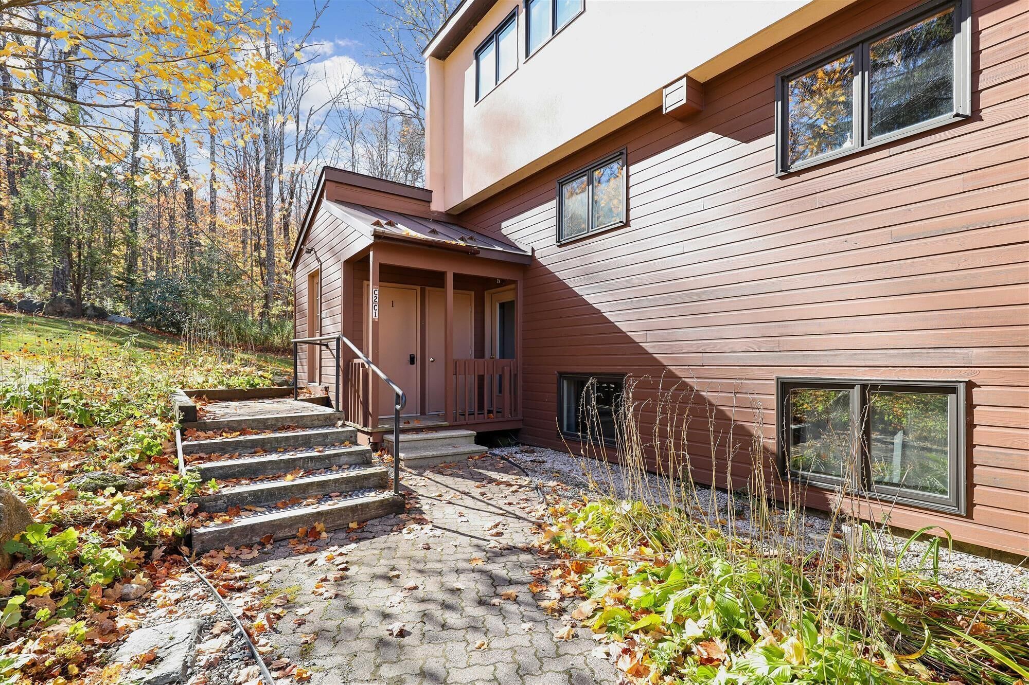 A modern two-story house with a wooden exterior, a covered porch, and a stone pathway leading to the entrance.