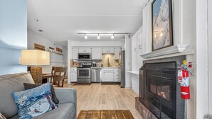Una sala de estar con chimenea, un sofá con un cojín decorativo, una mesa de centro y una cocina al fondo.