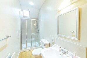 A modern bathroom with a glass-enclosed shower, a white toilet, and a sink with a mirror above it.