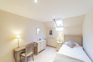 Ein Schlafzimmer mit Bett, Schreibtisch, Stuhl, Heizkörper und Fenster.