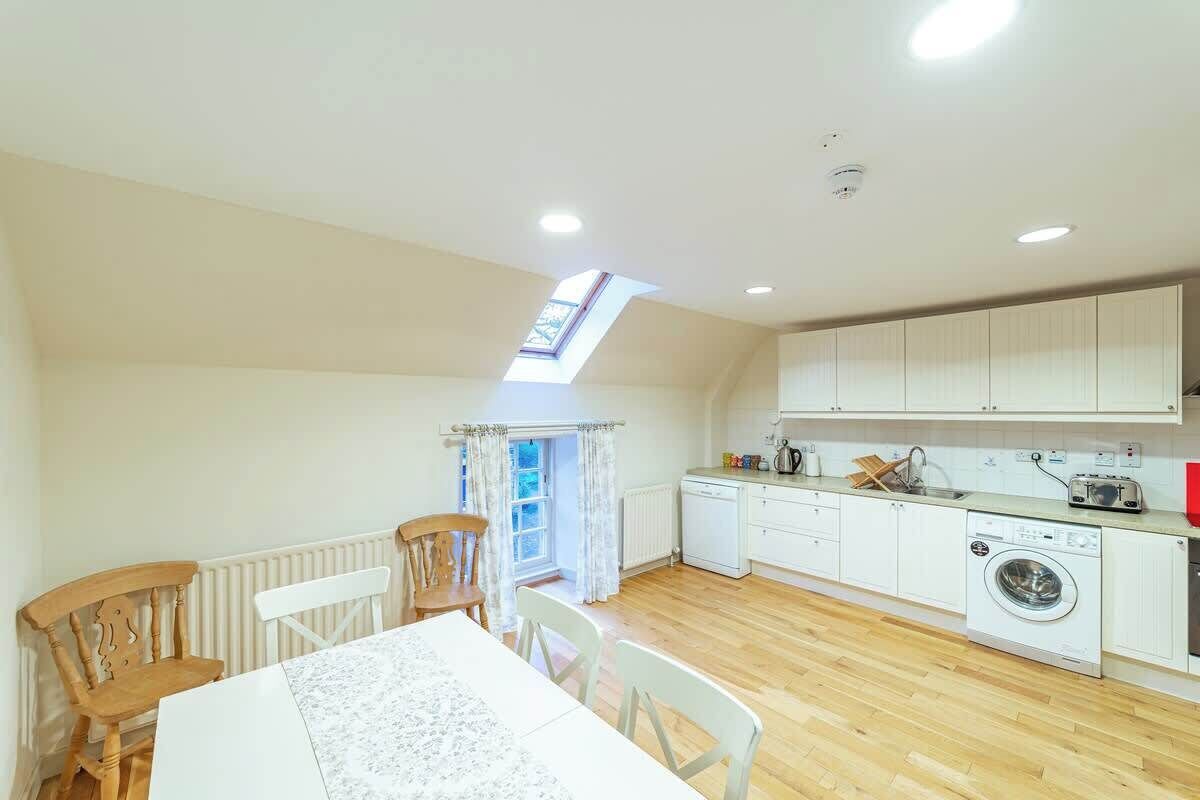 A compact kitchen with white cabinets, a washing machine, and a dining area with a table and chairs.