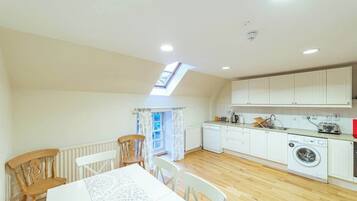 A compact kitchen with white cabinets, a washing machine, and a dining area with a table and chairs.