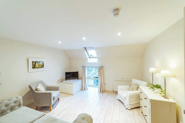 A spacious living room with a sofa, armchair, and a TV on a stand.