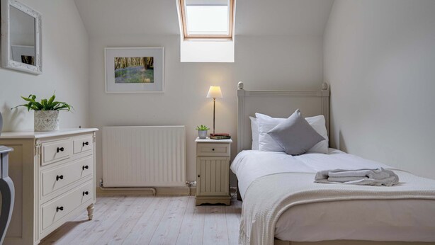 Et soveværelse med ovenlys, et sengebord med lampe, en radiator og en pænt redt seng.