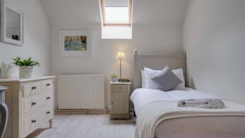 A bedroom with a skylight, a bedside table with a lamp, a radiator, and a neatly made bed.