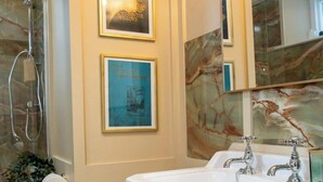 Ein Badezimmer mit einem weißen Waschbecken, zwei Wasserhähnen, einem Spiegel und gerahmten Bildern an der Wand.