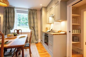 Una cocina compacta con armarios de madera, una mesa de comedor con sillas y una ventana con cortinas.