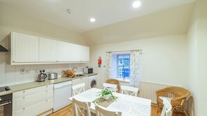 A compact kitchen with white cabinets, a dining table with chairs, a window with curtains, and a radiator. - Penninghame Estate - Bruce Apartment (Penninghame)