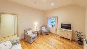 A spacious living room with a sofa, two armchairs, a TV, and a window with curtains. - Penninghame Estate - Bruce Apartment (Penninghame)