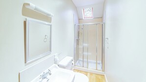 A modern bathroom with a large mirror, a sink, a toilet, and a glass-enclosed shower. - Penninghame Estate - Bruce Apartment (Penninghame)