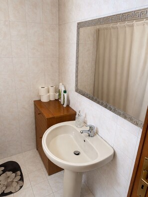 Un baño con lavamanos blanco, tocador de madera y espejo con detalles decorativos.