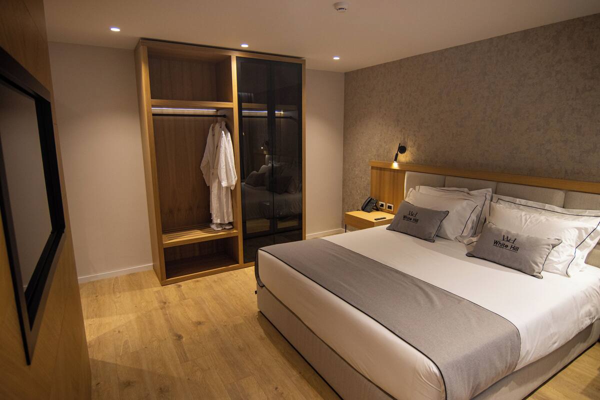 A bedroom with a large bed, a wooden wardrobe, a bedside table, and a nightstand.
