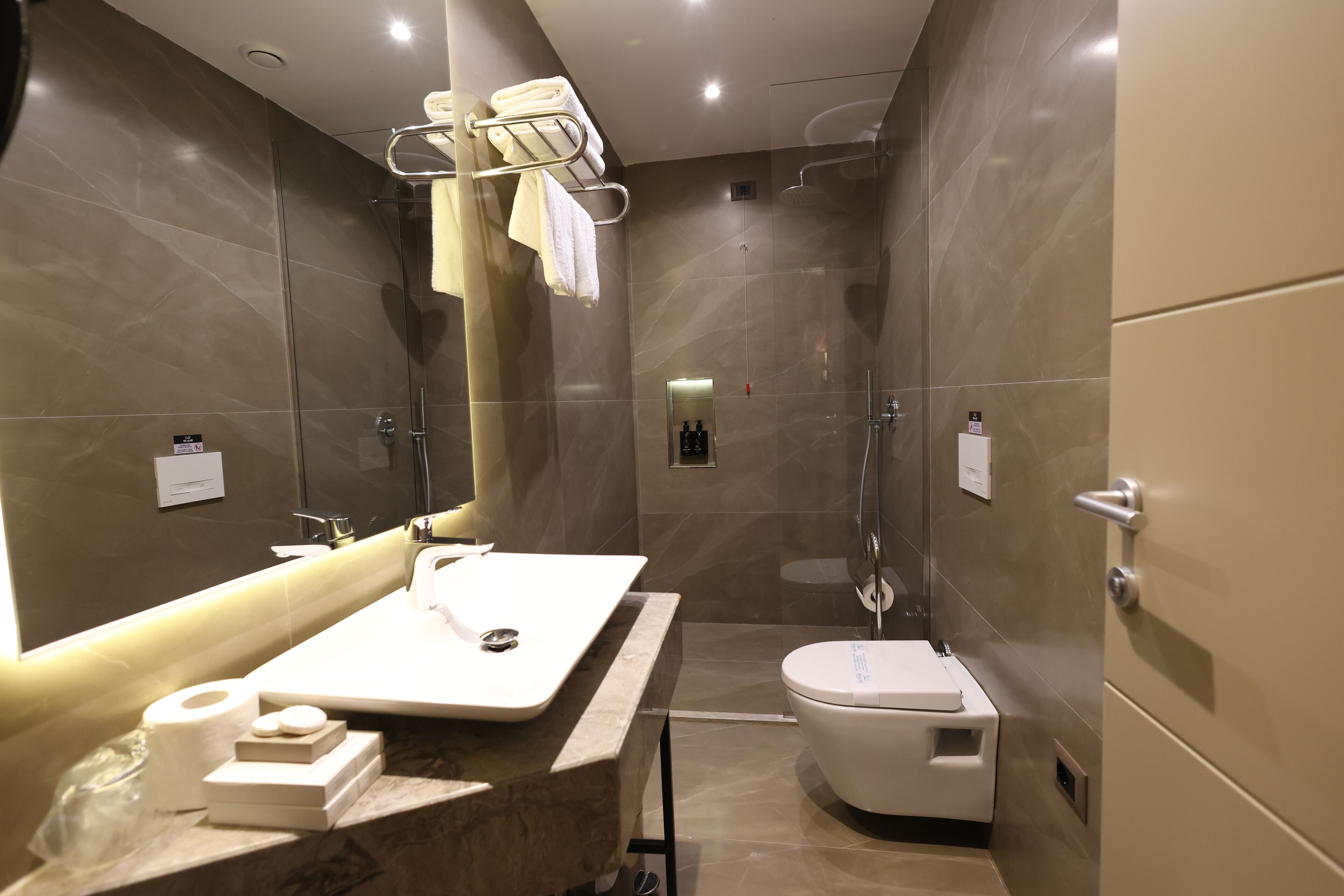 A modern bathroom with a large mirror, a sink, a toilet, and a shower.