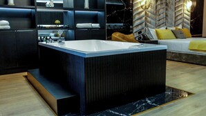 A modern bathroom with a large bathtub, a vanity with a mirror, and a seating area with a sofa and cushions. - White Hill Hotel Spa & Conference (Durres)