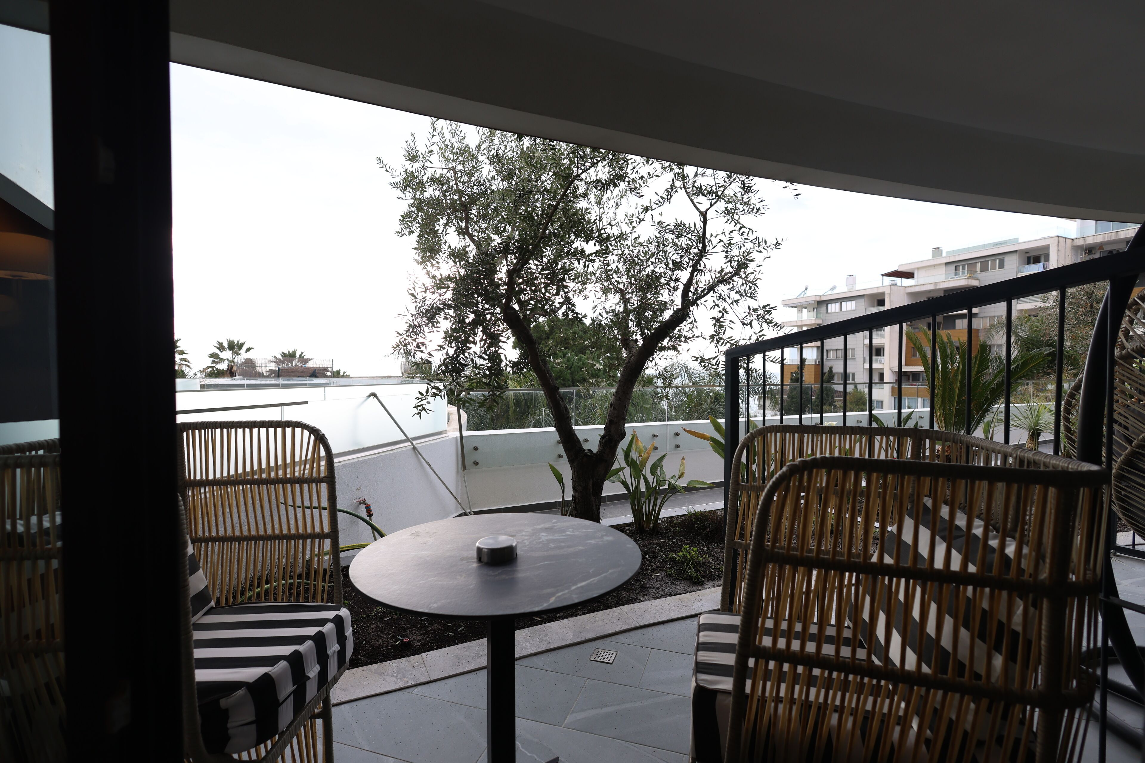 A balcony with wicker furniture, a round table, and a view of buildings and trees.