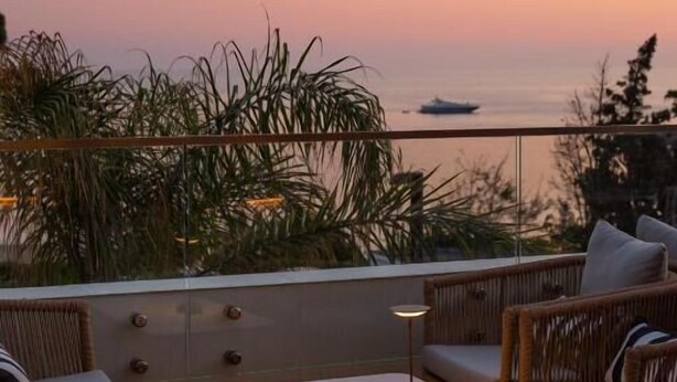 A balcony with wicker furniture, a table, and a view of the sea at sunset. - White Hill Hotel Spa & Conference (Durres)