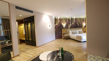 Habitación de hotel con cama, una mesa redonda con botellas, un sofá, un escritorio con una silla y un espejo grande.