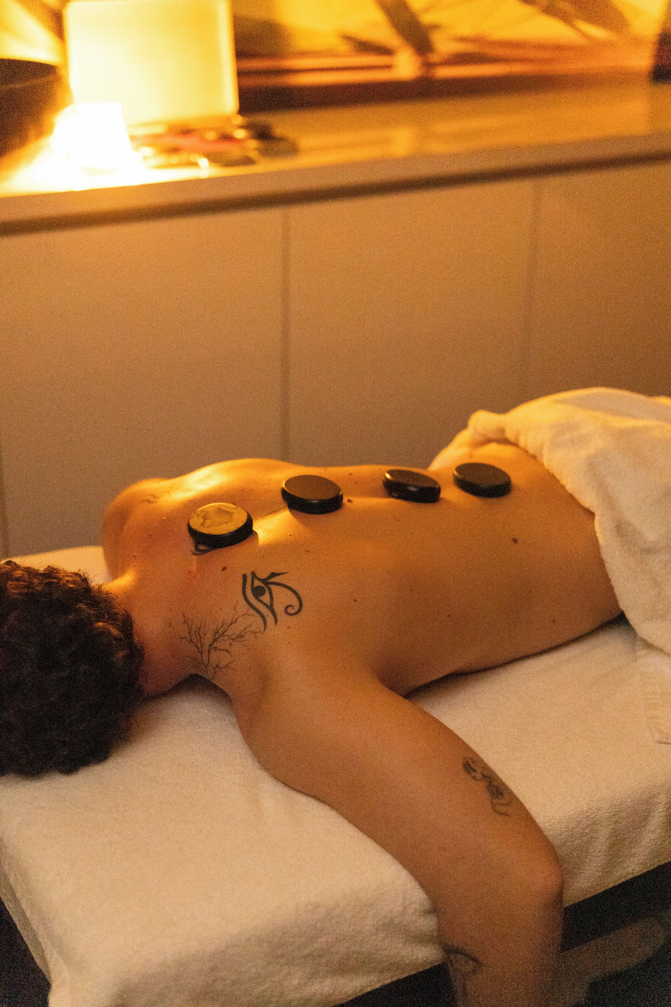 A person receiving a treatment with multiple black stones placed on their back.