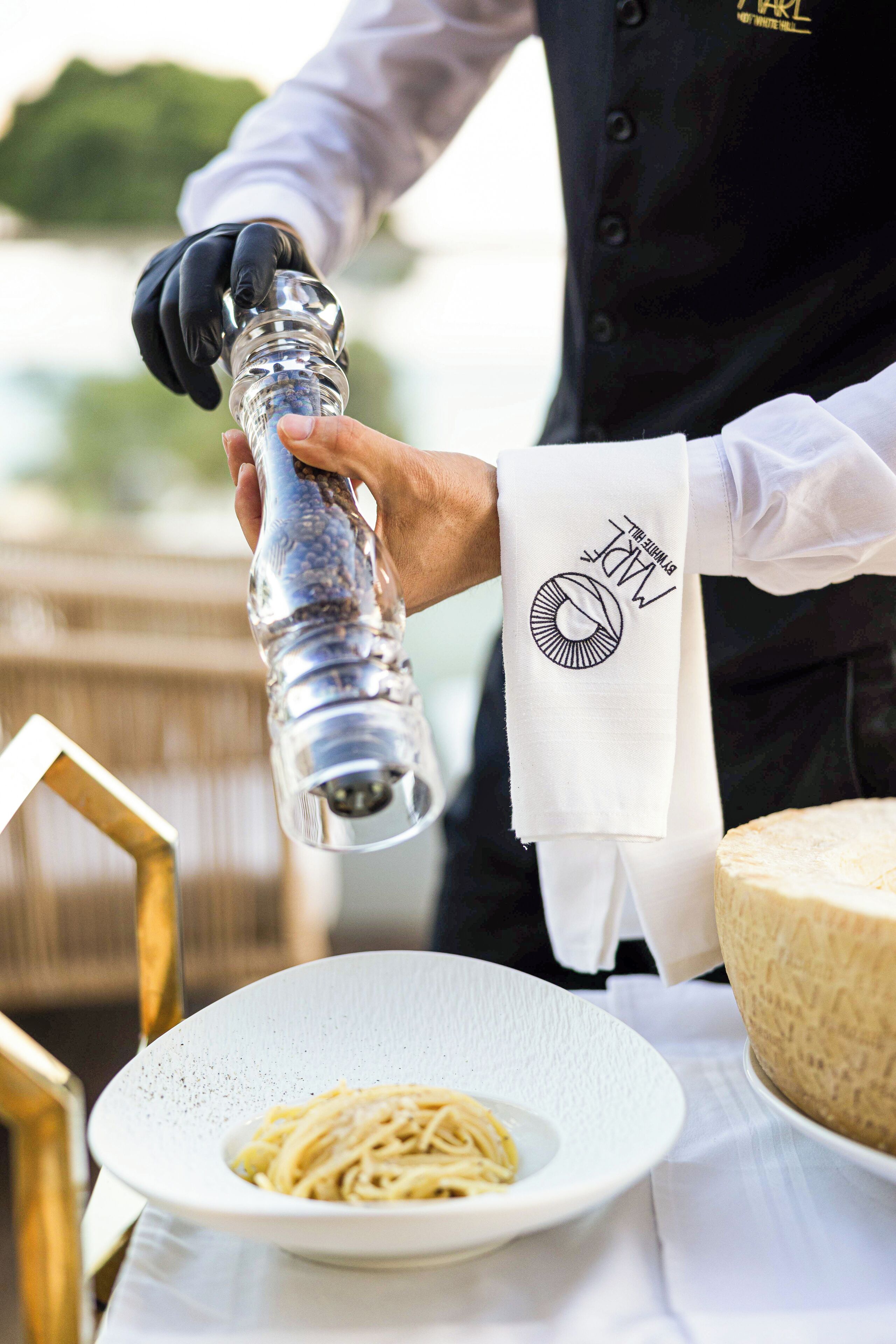A person pouring a liquid from a shaker into a plate of pasta.