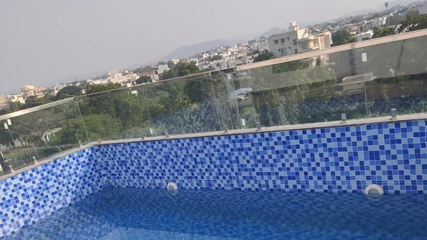 A swimming pool with blue mosaic tiles and metal handrails, surrounded by a cityscape with buildings and greenery. - Hotel Lake Heart  (Udaipur)
