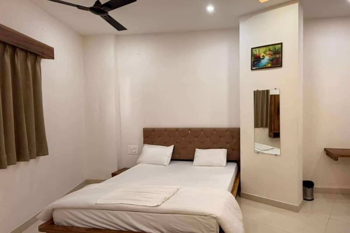 A bedroom with a bed, a ceiling fan, a wall-mounted mirror, and a painting.