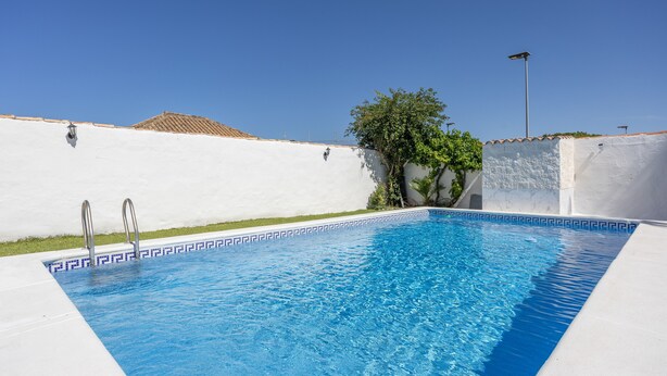 Ein Swimmingpool mit weiß gefliestem Rand, Metallhandläufen und blauem Himmel.