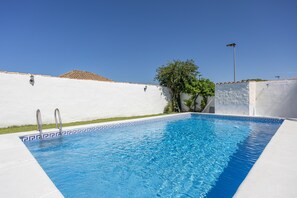 A swimming pool with a white tiled edge, metal handrails, and a clear blue sky.