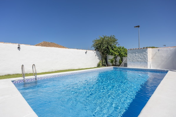 A swimming pool with a white tiled edge, metal handrails, and a clear blue sky.