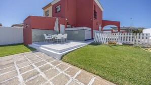 Ein rotes Haus mit Terrasse, weißem Zaun und kleinem Rasen.