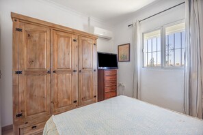 Une chambre à coucher avec un lit, une armoire en bois, une télévision et une fenêtre avec des rideaux.