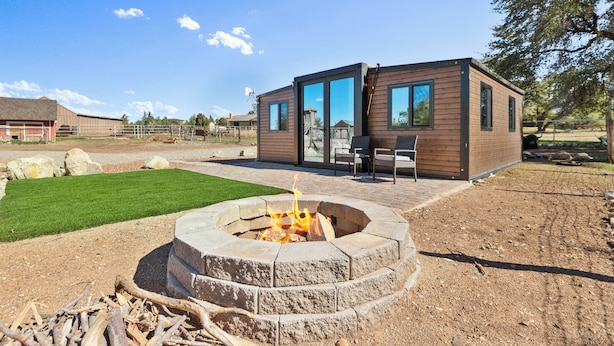 A modern outdoor living area with a fire pit, wooden deck, and a small building with glass doors.