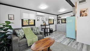 A modern living room with a grey sofa, a wooden coffee table, and a kitchen area with a light blue refrigerator.