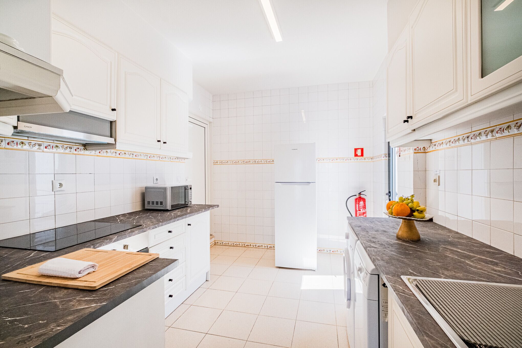 A modern kitchen with white cabinets, a microwave, a toaster, and a fruit bowl on the counter.