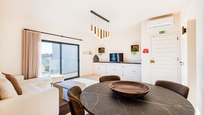 Un salon moderne comprenant un canapé, une table à manger avec un saladier, et un coin cuisine avec une télévision et des placards.