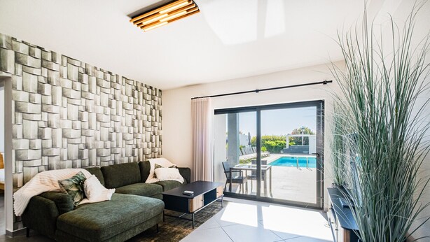 Un salon moderne avec un mur au motif de pierres, un canapé vert, une table basse et une vue sur une piscine, visible à travers de grandes portes vitrées.