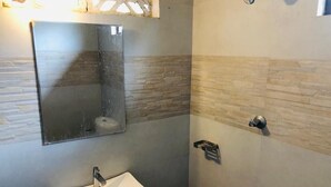 Un baño con lavamanos blanco, espejo y zona de ducha con pared de azulejos.