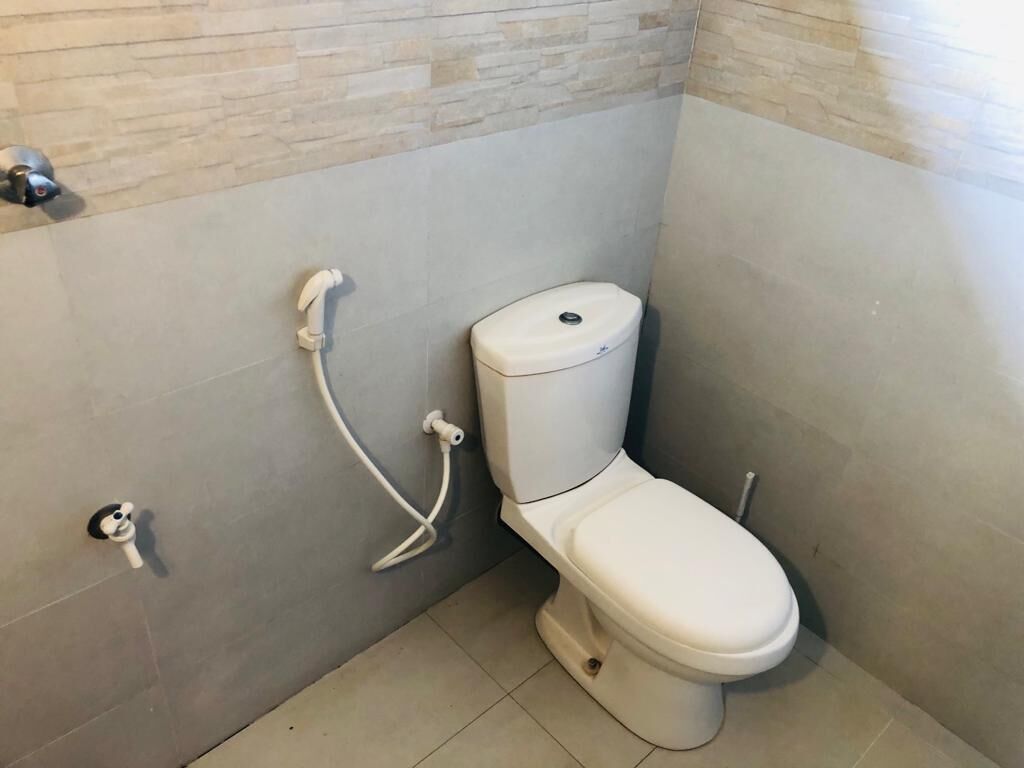 A small, modern bathroom with a toilet, a hand dryer, and a wall-mounted flush handle.