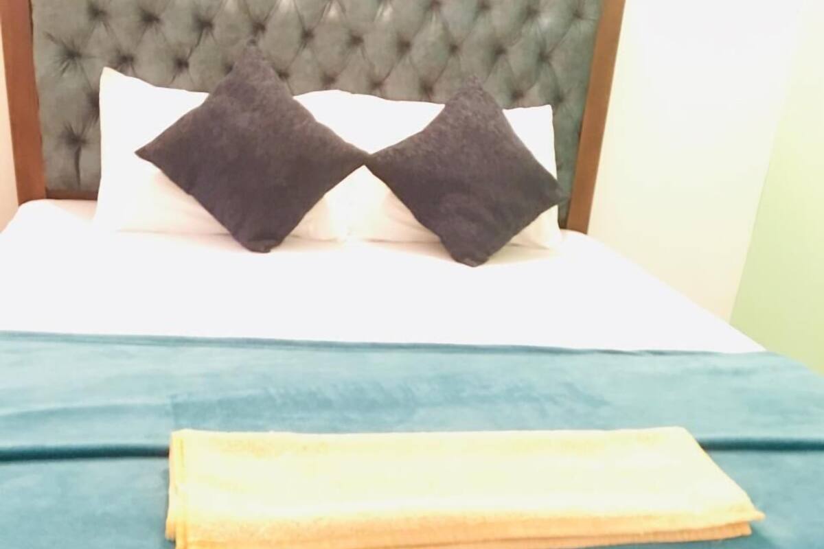A bed with a tufted headboard, two dark pillows, and a folded yellow blanket.