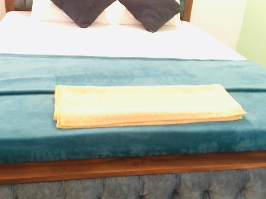 A bed with a tufted headboard, two dark pillows, and a folded yellow blanket.
