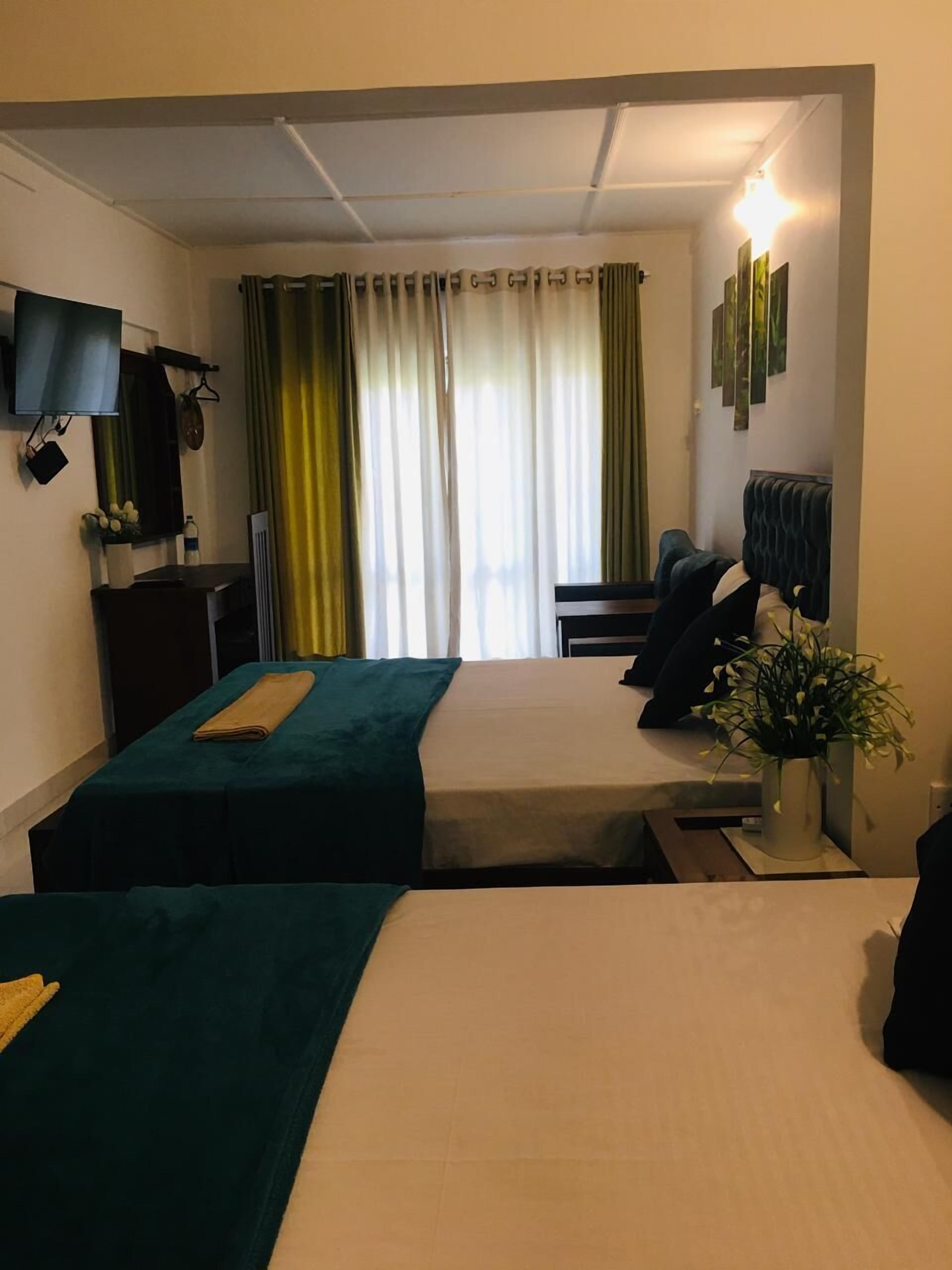 Une chambre d’hôtel avec deux lits, un bureau, une télévision et une fenêtre avec des rideaux.
